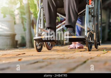 donna anziana in sedia a rotelle che cammina con l'operatore sanitario Foto Stock