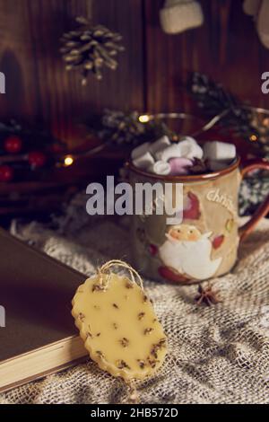 Una fragrante bustina fatta a mano in cera d'api e una tazza con cacao sullo sfondo di un arredamento di Capodanno. Foto Stock