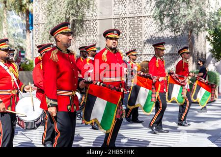 Dubai, Emirati Arabi Uniti, 09.12.2021. Orchestra della fascia di Ottone della polizia degli Emirati che suona all'Expo 2020 Dubai Daily Parade, uomini vestiti in suite rosse che trasportano la nazione degli Emirati Foto Stock