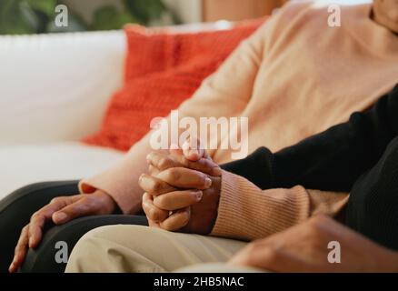 Primo piano di una coppia multiculturale di anziani che tiene le mani sul divano del soggiorno Foto Stock