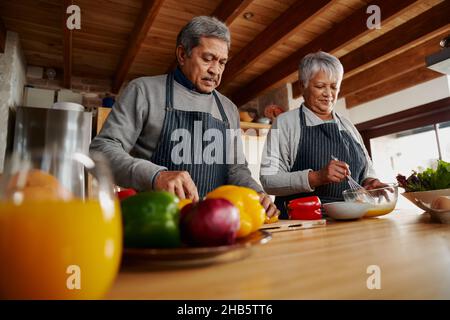 Coppia anziana biraciale che cucinano felicemente in cucina. Marito e moglie che vivono sano stile di vita in pensione. Foto Stock