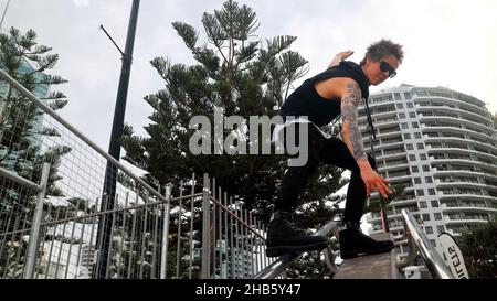 Bel ragazzo tatuato con occhiali da sole e capelli spiky surf sulle corrimano scala in Surfers Paradise, Gold Coast, Australia. Foto Stock