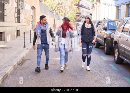 Pieno corpo di amici multietnici maschi e femmine in elegante abbigliamento casual a piedi su strada asfaltata passando le auto e di avere conversazione Foto Stock