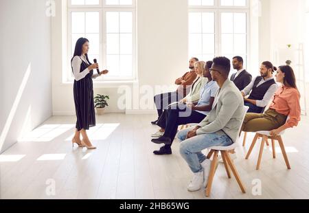 Altoparlante femmina che tiene un microfono e che dà una lezione per giovani diversi Foto Stock