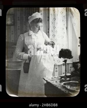 Slide di lanterna magica di infermiera in uniforme che tiene il bambino neonato all'interno di una casa, Inghilterra, Regno Unito c 1900-1910 Foto Stock