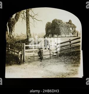 Magic lanterna scivola di bambini da cancello ingresso con misterioso aspetto edera coperto casa in piedi su smack collina in campo dietro, Inghilterra, Regno Unito c 1900- 1910 Foto Stock