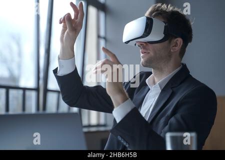 Un uomo entusiasta che indossa occhiali di protezione per la realtà virtuale che tocca oggetti con le mani nel mondo digitale Foto Stock