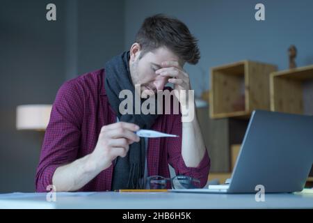 Un uomo austriaco infelice che controlla la temperatura corporea al lavoro, mantenendo il termometro Foto Stock