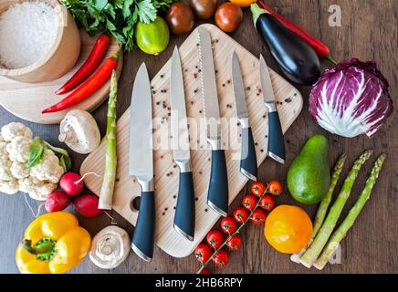 Chef Knifes su bordo di tritare in legno con verdure fresche sfondo. Concetto di cibo sano. Cibo vegetariano crudo Foto Stock