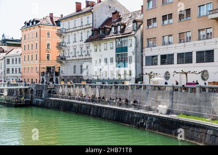 Lubiana, Slovenia - 04 07 2018: Giovani seduti su terrazze soleggiate lungo le rive del fiume Lubiana Foto Stock