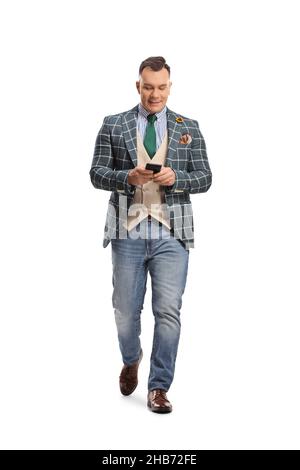 Ritratto a tutta lunghezza di un uomo in abito elegante e jeans a piedi e utilizzando uno smartphone isolato su sfondo bianco Foto Stock