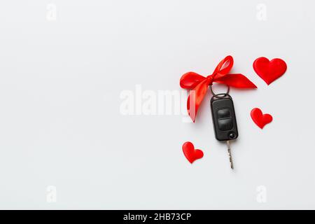 Chiave auto con arco rosso e un cuore su un tavolo colorato. Regalo o regalo per San Valentino o natale, vista dall'alto con spazio per le copie. Foto Stock