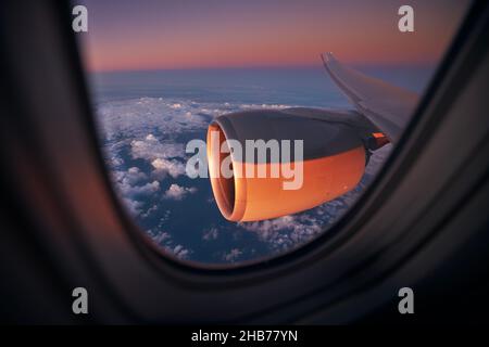 Vista dalla finestra dell'aeroplano durante il volo sopra l'oceano alla splendida alba. Focalizzazione selettiva sul motore a reazione. Foto Stock