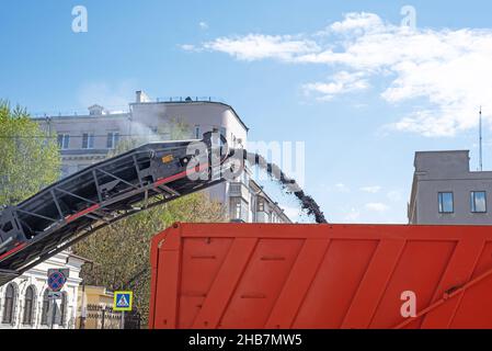 La fresatrice per asfalto riempie il dumper con la vecchia pavimentazione Foto Stock