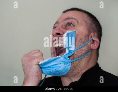Primo piano di un uomo stanco di indossare la maschera. Andato pazzo, lui lo snatches Foto Stock