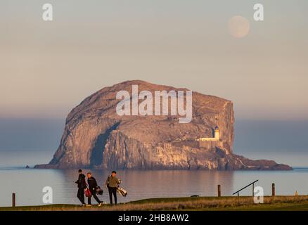 North Berwick, East Lothian, Scozia, UK, 17th dicembre 2021. UK Meteo: La luna piena sorge su Bass Rock. La luna piena di dicembre è chiamata "Luna fredda". Oggi è salito poco prima del tramonto. Nella foto: I golfisti possono godersi un'ultima partita prima che il sole tramonti sul campo da golf di Glen Foto Stock