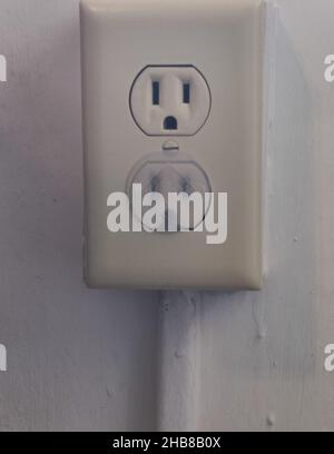 Due prese elettriche, quella inferiore coperta da una spina di sicurezza per bambini, e quella superiore no. Foto Stock