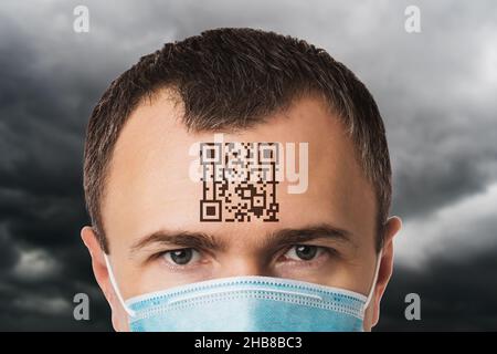 Un uomo in maschera con un codice QR sulla fronte, sullo sfondo di un cielo nuvoloso, un concetto sul tema di una prigione digitale a causa del coronavirus, Foto Stock