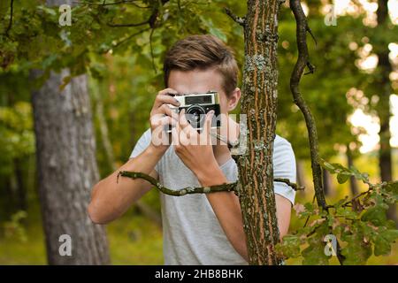 Chernihiv, Ucraina - 26 luglio 2019: Un ragazzo nella foresta scatta foto con una vecchia macchina fotografica Foto Stock