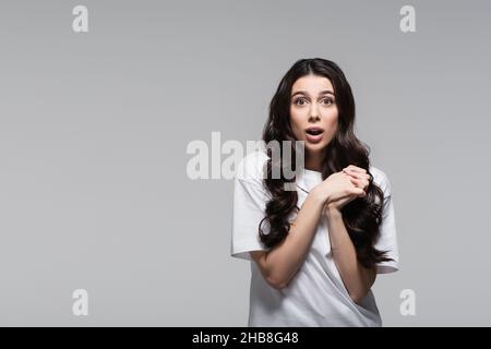 donna sorpresa con lunghi capelli ondulati e mani argillate isolate sul grigio Foto Stock