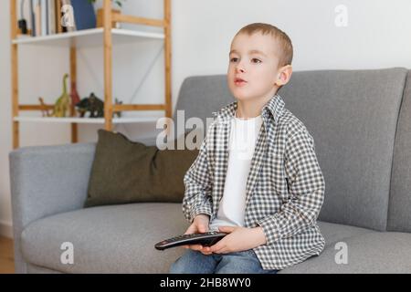 Telecomando TV per bambini. Ragazzo senza controllo genitori guardando la televisione. Istruzione della prima infanzia e tempo libero in età elementare. Foto Stock