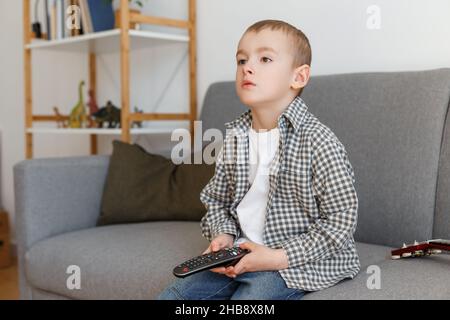 Telecomando TV per bambini. Ragazzo senza controllo genitori guardando la televisione. Istruzione della prima infanzia e tempo libero in età elementare. Foto Stock