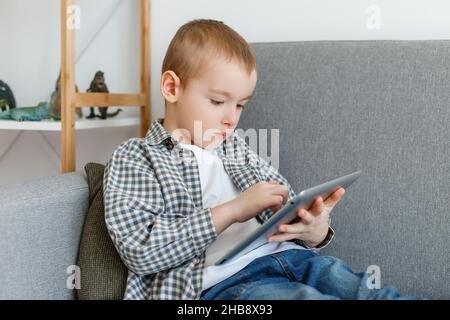 Ragazzo senza controllo parentale perdere tempo a giocare ai giochi. Bambino che si diverte con il tablet. Istruzione della prima infanzia e tempo libero in età elementare Foto Stock