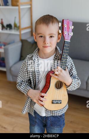 Capretto di talento che tiene il soprano ukulele nel paese. Ragazzo prescolare che impara la chitarra a piacere. Concetto di educazione della prima infanzia e hobby musicale Foto Stock