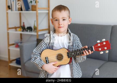 Capretto di talento che tiene il soprano ukulele nel paese. Ragazzo prescolare che impara la chitarra a piacere. Concetto di educazione della prima infanzia e hobby musicale Foto Stock