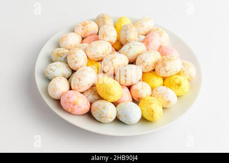 Caramelle miste ricoperte di cioccolato per le uova di Pasqua su un piccolo piatto isolato su un tavolo bianco, gustoso dessert zuccherato per i bambini Foto Stock