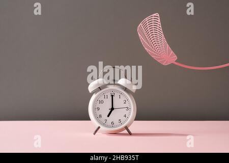 Sbattendo una sveglia con un mosca swatter - concetto di non volontà di alzarsi al mattino Foto Stock