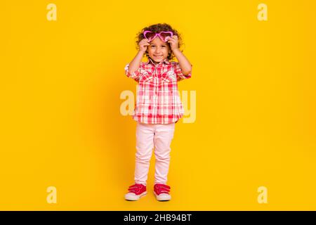 Foto di carino scuola ragazza vestita vestiti a scacchi braccia occhiali cuore sorridente isolato colore sfondo giallo Foto Stock