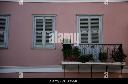 Vecchia facciata neoclassica casa con una parete di stucco rosa salmone, persiane finestre in legno grigio e una ringhiera in ferro artigianale balcone a Koroni, in Grecia. Foto Stock