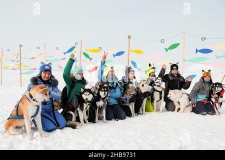 Dudinka, Krasnoyarsk Territory, Russia, 13 aprile 2019: Un grande gruppo di persone con cani Husky per slittino si siedono nella neve e sorridono. Foto Stock