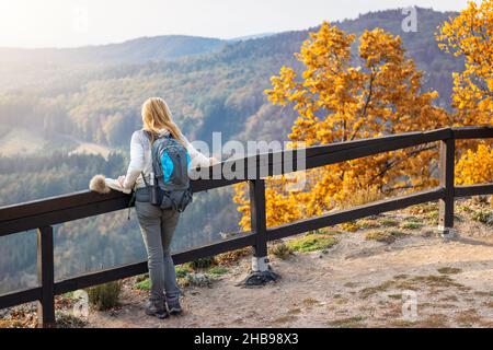 Donna escursionista che gode di vista sulla montagna nella stagione autunnale. Escursioni nella foresta con foglie di colore arancione. Donna con zaino che indossa abiti caldi Foto Stock