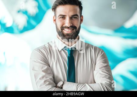 Ritratto di riuscito uomo d'affari caucasico bearded con camicia e cravatta in piedi con le braccia incrociate in ufficio. Sul polso orologio da polso. Affamate il vostro distrac Foto Stock