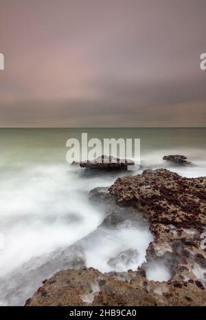 onde che si infrangono su rocce sull'isola di wight shoreline, astratto generico mare di costa con rocce aspre e vorticoso mare lattiginoso, costa astratta. Foto Stock