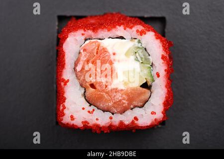Rotolo giapponese fatto in casa con salmone, cetriolo, formaggio cremoso e caviale rosso su sfondo nero vista dall'alto Foto Stock