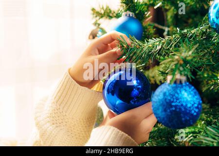 Natale e Capodanno concetto, albero di Natale a casa fesivamente decorato su uno sfondo sfocato fata luminosa. Si possono vedere le mani di una ragazza giovane Foto Stock