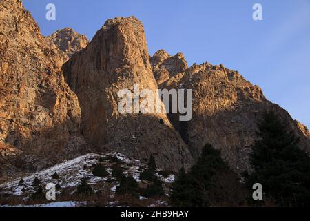 Enormi montagne rocciose con neve e alberi nella gola di Tuyuksu al tramonto in autunno Foto Stock