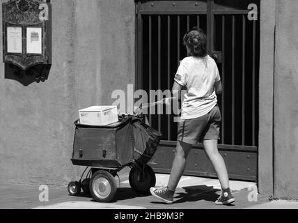 Una lavoratrice postale femminile consegna posta e pacchi nel centro di Santa Fe, New Mexico, utilizzando un carrello a ruote. Foto Stock