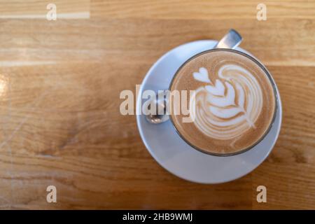 Outdoor Vintage Mood, Cappuccino in cima con cuore fiore latte art adagiare su texture tavolo in legno. Ama l'arte del latte sul cappuccino al caffè. Foto Stock