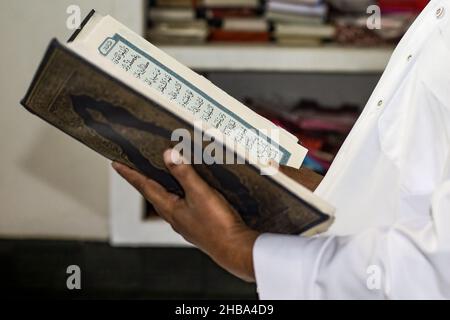 Uomo musulmano che legge il libro sacro del corano all'interno della moschea Foto Stock