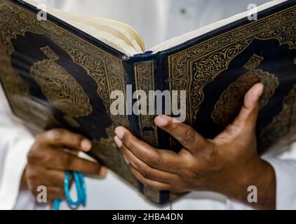 Vista ravvicinata di una mano che tiene aperto il libro al quran con focus selettivo Foto Stock