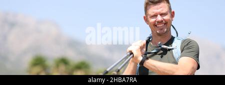 Uomo sorridente che tiene i bastoni scandinavi in cima al primo piano di montagna Foto Stock