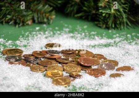 Monete d'oro giacenti sulla neve sullo sfondo di rami di abete rosso verde, primo piano, fuoco selettivo. Concetto di successo. Concetto di risparmio. Conc. Ricchezza Foto Stock