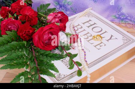 Rose con Bibbia e anelli di nozze su tavola di legno Foto Stock