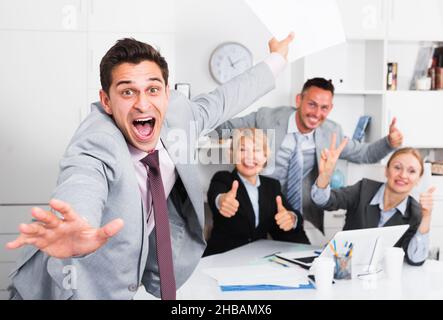 Un uomo d'affari entusiasta con un team felice che celebra la vittoria Foto Stock