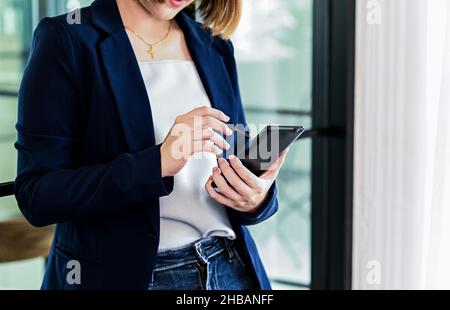 Le donne d'affari si mano con la matita utilizzando sullo smartphone, donna in un vestito in piedi da una finestra con una matita utilizzando uno smartphone, primo piano scatto con a s. Foto Stock