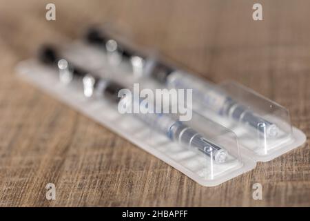 Un ritratto di una confezione con due siringhe adagiate su un tavolo di legno. I shot di farmaco per iniezione sono costituiti da un tubo di vetro con segni di volume su Foto Stock